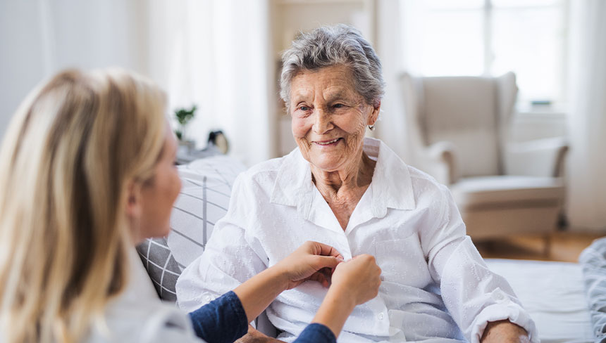 Eine weibliche Pflegekraft hilft einer älteren Dame beim Zuknüpfen der Bluse