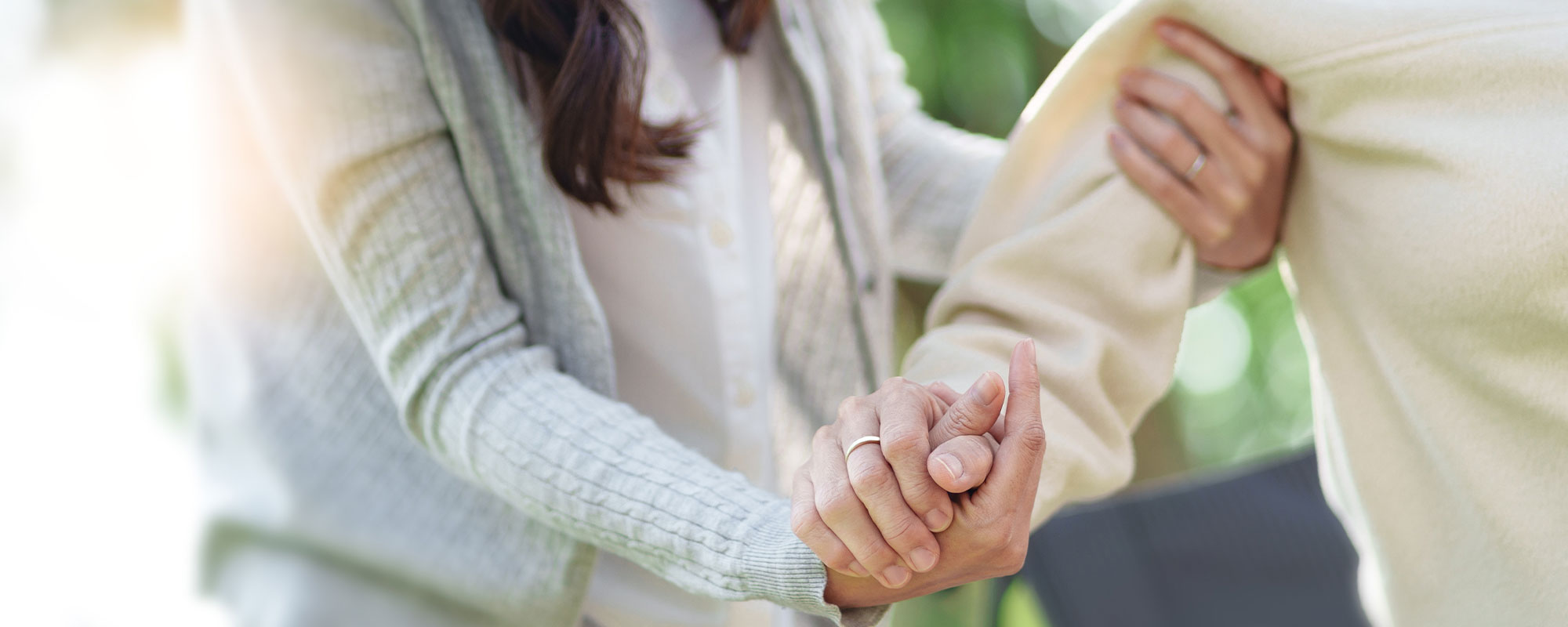 Eine weibliche Pflegekraft stütz eine ältere Frau und hält ihr zur Unterstützung die Hand